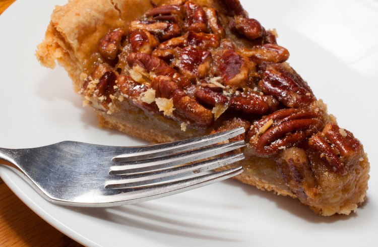 Sticky sweet pecan pie on a plate with a fork