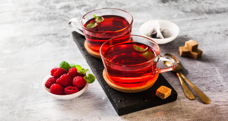 hot raspberry tea in two transparent cups on a stone table. Fresh berries, cubes of cane sugar and a bag of tea